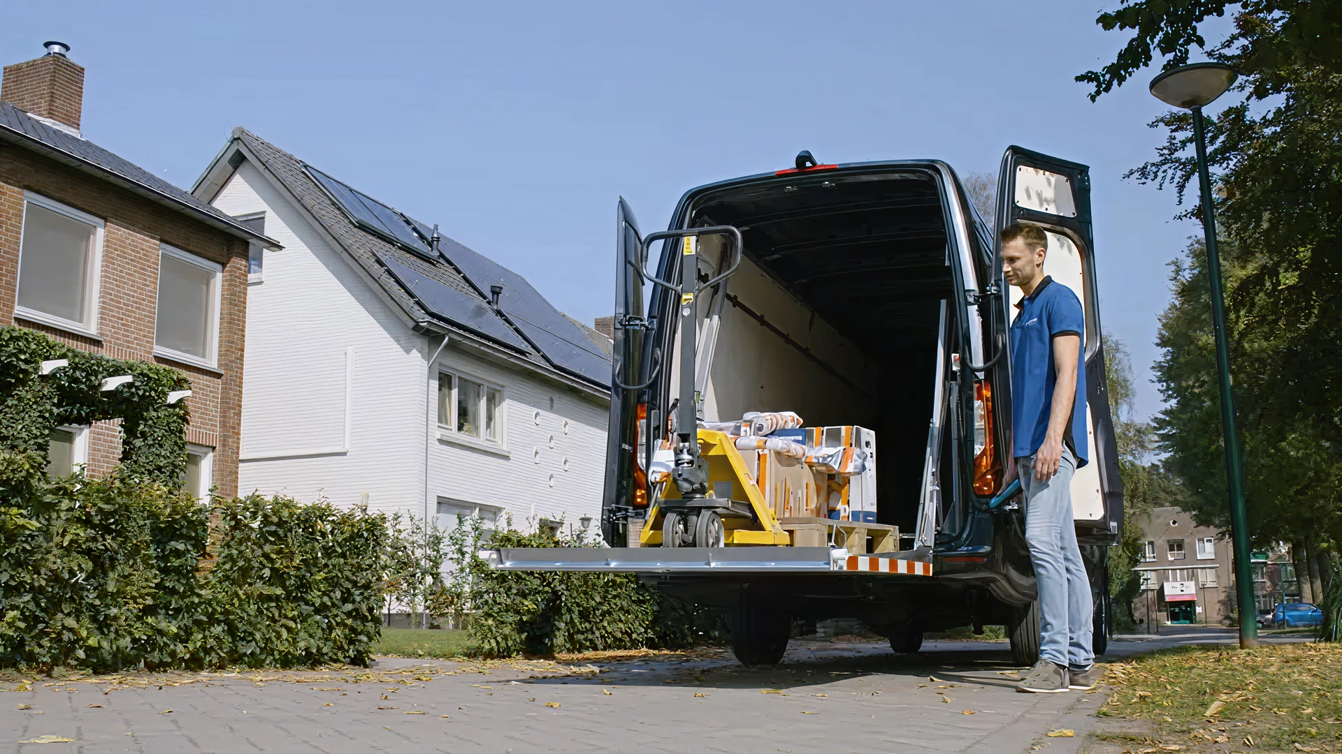 Man laad EasyLoader‑laadklep uitklappen van een bestelbus pallet met goederen te lossen bij een woonhuis.